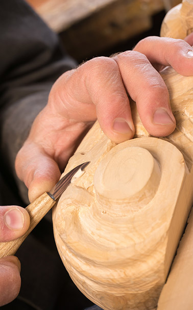A man hand-carving an intricate shape in wood